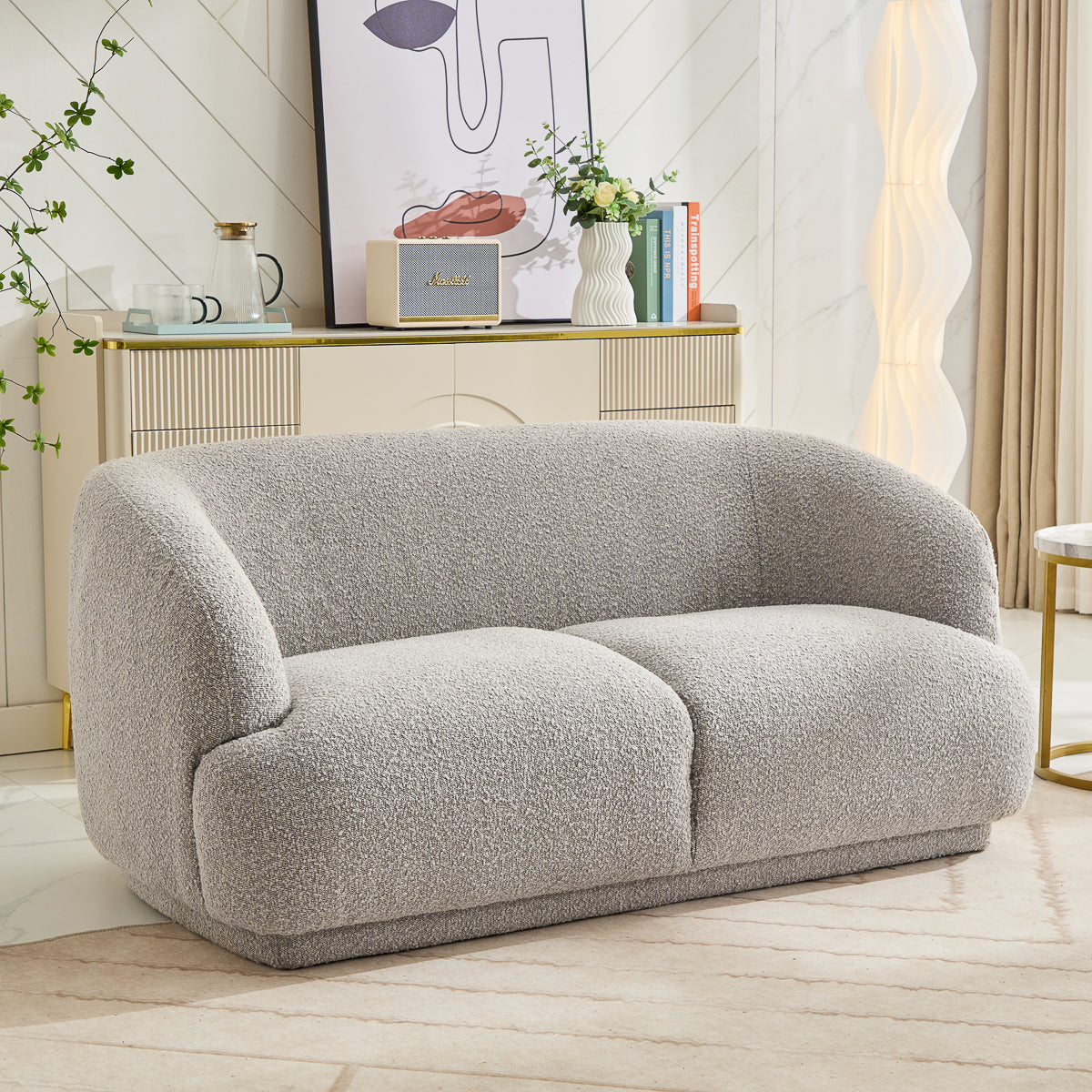 A modern living room features the Avriio Madrid 2 Seater Taupe Sofa on a beige rug, paired with a console table displaying books and art. Cream curtains add warmth, and White Glove Options provide seamless home delivery for this inviting space.
