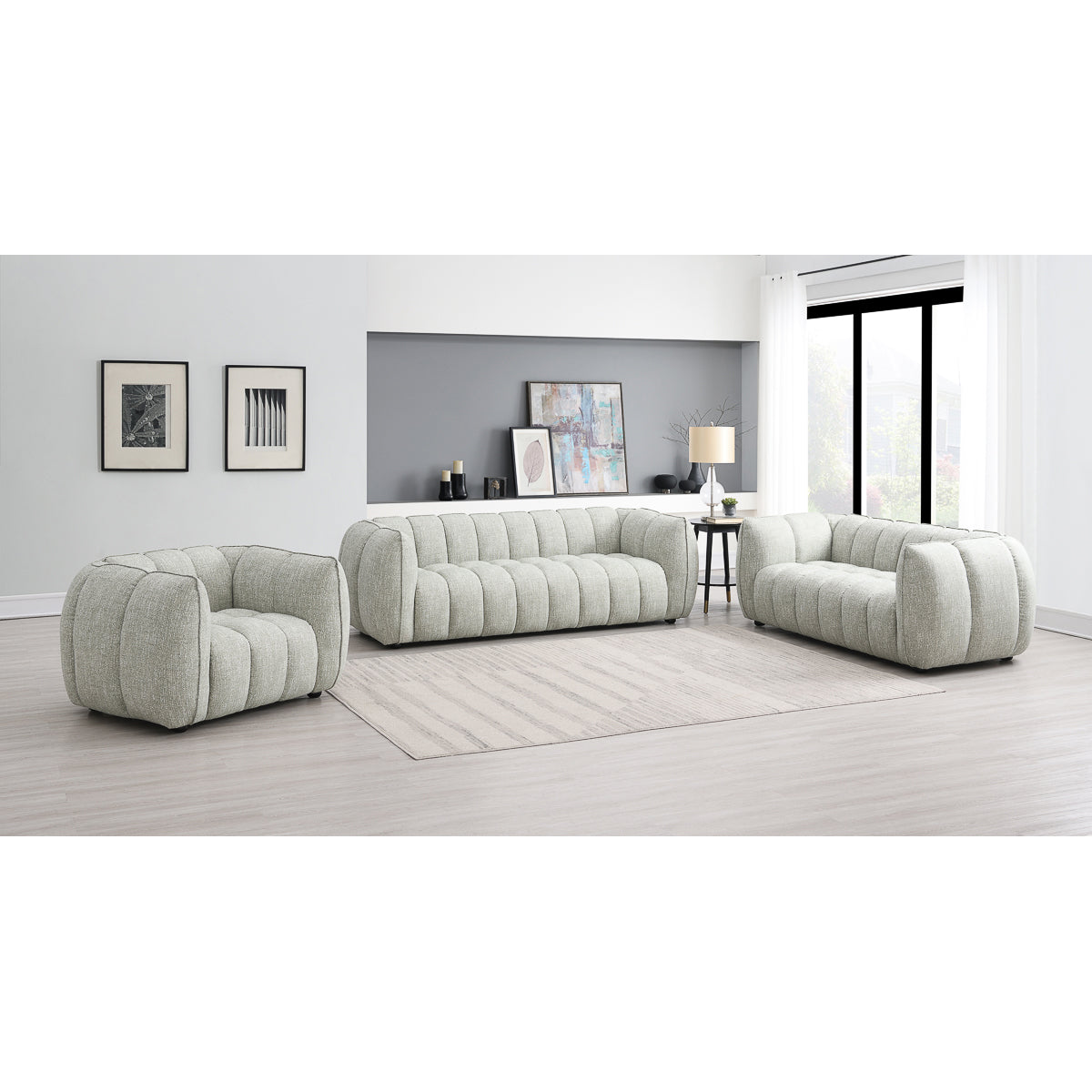 A modern living room featuring the Avriio Vienna Fluted Arm Chair in pale green fabric, a large beige rug, minimalist decor, wall art, shelves, a lamp, and bright windows with sheer white curtains—White Glove Home Delivery available.